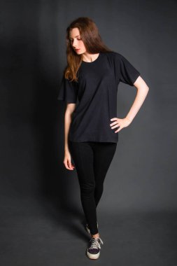 Güzel, uzun saçlı, siyah elbiseli, gri arka planda stüdyoda poz veren genç bir kadın. Temiz ciltli bir model..