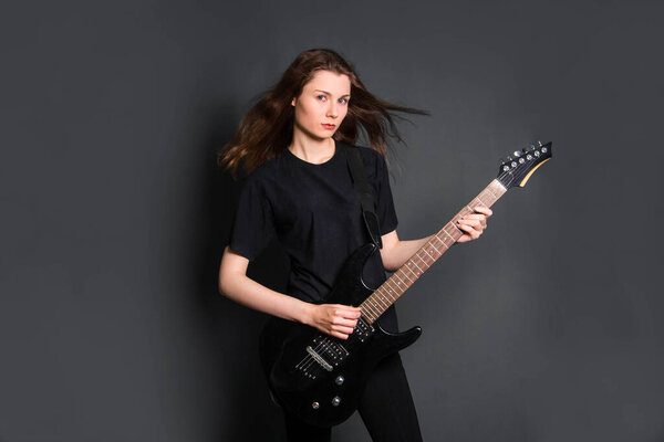 Портрет красивой, молодой рок-женщины в черной одежде с электрогитарой в руках. Студийное фото на сером фоне. Модель с чистой кожей
.