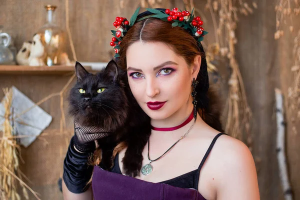 一个年轻貌美的巫婆的画像 她有一只大大的黑猫 背景是炼金术士 小瓶和干草 — 图库照片