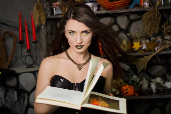 一个穿着黑色紧身衣 手里拿着一本书的年轻漂亮的巫婆在念咒语 工作室的照片 穿着万圣节服装的女孩 皮肤洁白的模特 — 图库照片
