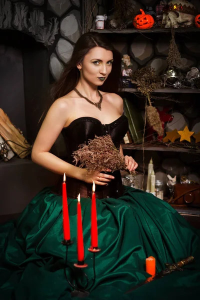 一个穿着绿色裙子和黑色紧身衣的年轻漂亮的女人坐在地板上 手里拿着一把点燃的蜡烛 手里拿着一把刀 女巫会变魔术的万圣节 — 图库照片