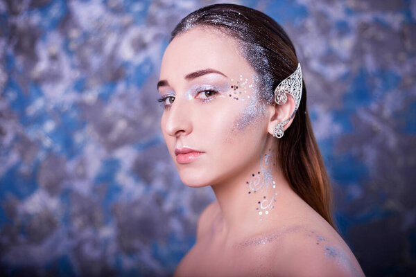 Closeup beauty portrait of a woman with an earring on her ears. Studio photo on speckled, colorful background. Model with clean skin, retouching, makeup. The concept of elven beauty.