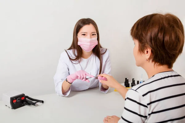 Vrouw Een Manicure Een Witte Jas Masker Handschoenen Snijdt Nagels — Stockfoto