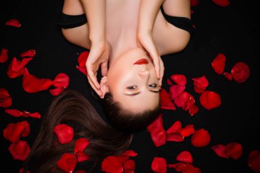 Siyah arka plan ve gül yaprakları üzerinde yatan bir kızın portresi. Sevgililer Günü konsepti.