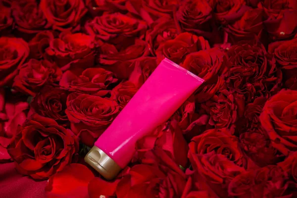 A pink tube of cream, branding mockup, lies in red roses.