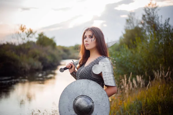 川や夕日を背景に剣と盾を手にした鎖状の郵便で中世の女性戦士の肖像画 戦闘メイク クリアスキン レタッチ — ストック写真