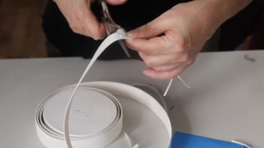 Tıbbi maske takmak için elastik bant kesen kadınların ellerini kapatın. Koronavirüs salgını sırasında maske dikmek. Koruyucu maske eksikliği kavramı.