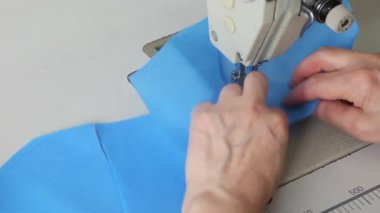 Dikiş makinesindeki mavi kumaştan tıbbi maskeler aşamalı olarak dikilmiş. Endüstriyel dikiş makinesi kapanıyor. Koronavirüs salgını sırasında tıbbi maske eksikliği konsepti.