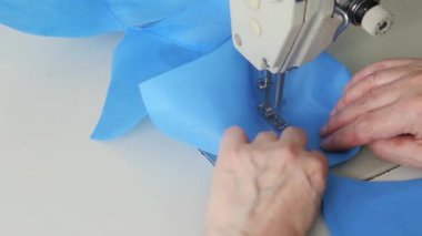 Dikiş makinesindeki mavi kumaştan tıbbi maskeler aşamalı olarak dikilmiş. Endüstriyel dikiş makinesi kapanıyor. Koronavirüs salgını sırasında tıbbi maske eksikliği konsepti.