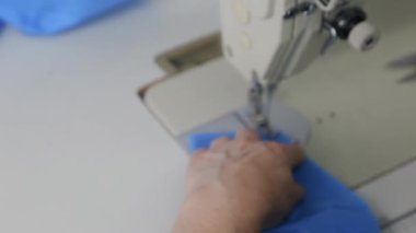 Dikiş makinesindeki mavi kumaştan tıbbi maskeler aşamalı olarak dikilmiş. Endüstriyel dikiş makinesi kapanıyor. Koronavirüs salgını sırasında tıbbi maske eksikliği konsepti.