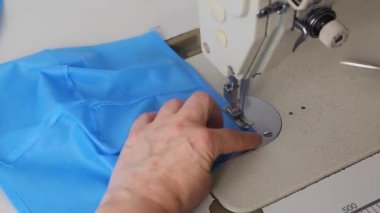 Dikiş makinesindeki mavi kumaştan tıbbi maskeler aşamalı olarak dikilmiş. Endüstriyel dikiş makinesi kapanıyor. Koronavirüs salgını sırasında tıbbi maske eksikliği konsepti.