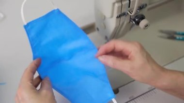 Dikiş makinesindeki mavi kumaştan tıbbi maskeler aşamalı olarak dikilmiş. Endüstriyel dikiş makinesi kapanıyor. Koronavirüs salgını sırasında tıbbi maske eksikliği konsepti.