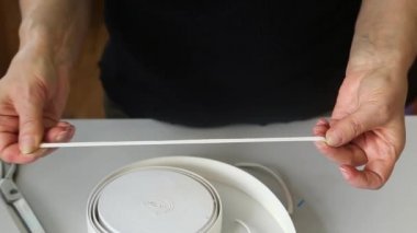  Yakın plan, yeniden kullanılabilir yüz maskeleri üretimi için elinde elastik bir bant tutan bir kadın. Koronavirüs salgını sırasında tıbbi maske sıkıntısı..