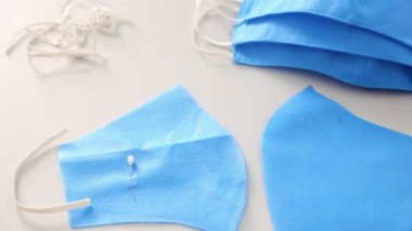 Kesmek ve dikmek için masanın üzerindeki kameranın düzgün hareketi, bitmemiş maskeden bitmiş maskeye ve mavi kumaşın üzerinde yatan makasa odaklanmayı değiştirdi. Maske dikme kavramı.