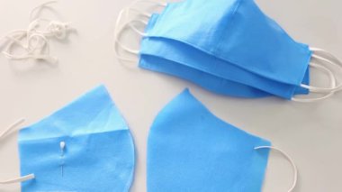 Kesmek ve dikmek için masanın üzerindeki kameranın düzgün hareketi, bitmemiş maskeden bitmiş maskeye ve mavi kumaşın üzerinde yatan makasa odaklanmayı değiştirdi. Maske dikme kavramı.