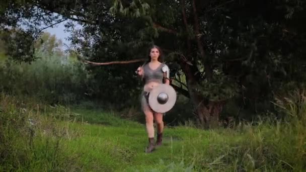 中世の女性戦士は盾と剣を手に鎧を着て森から道を歩く モデルはフレームを離れる — ストック動画