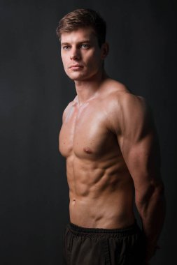 Kaslı vücut geliştirici, siyah arka planda çıplak bir gövdeyle poz veriyor. Seksi adam..