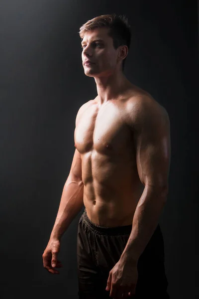 バックライト付きの暗闇の中で黒の背景に裸の胴を持つ筋肉のボディビルダーのポーズ セクシー男 — ストック写真