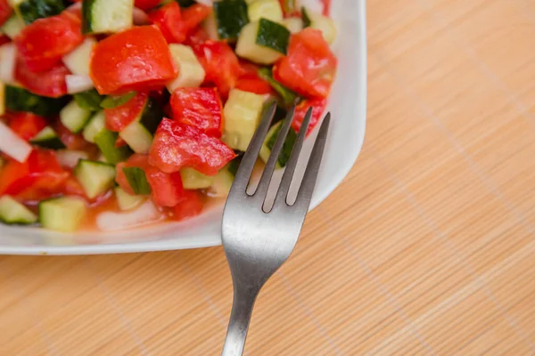 用新鲜的 切碎的蔬菜 西红柿和洋葱做成的蔬菜沙拉 用葵花籽油放在白盘里 叉子放在木桌上 健康饮食和素食的概念 — 图库照片