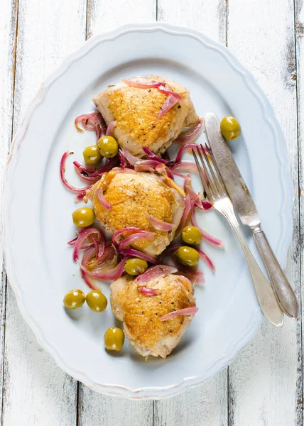 Kavrulmuş tavuk uyluk zeytin ve beyaz tahta üzerinde kırmızı soğan ile