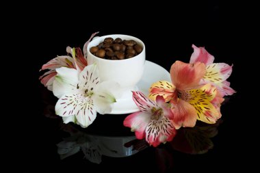 Siyah arka planda kahve taneleri olan bir fincan beyaz kahve. Fincanın etrafında güzel çiçekler var.