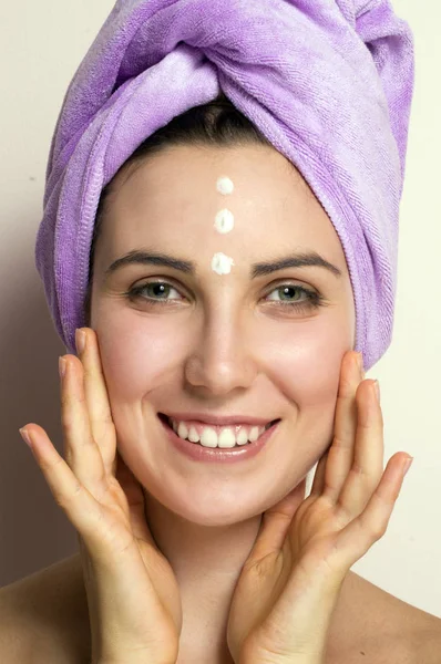 Foto Mujer Joven Toalla Púrpura Cabeza Usando Crema Facial Sobre —  Fotos de Stock