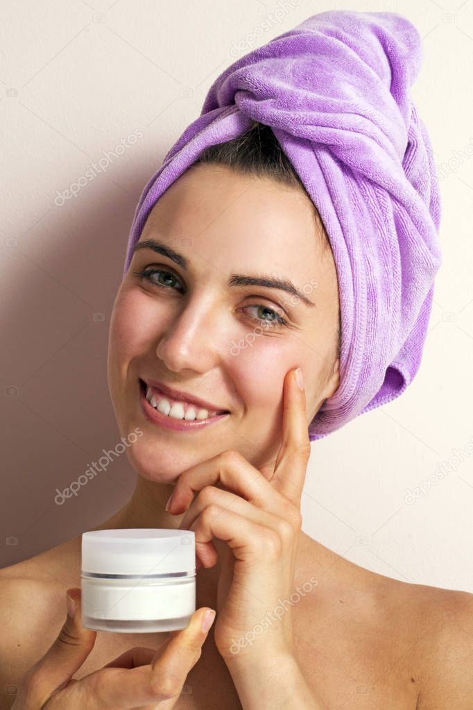 photo of young woman in purple towel on head holding face cream on pink background