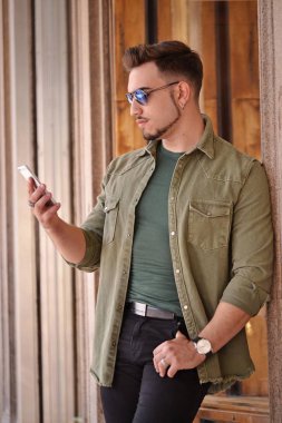 Açık havada yapısı arka plan üzerinde cep telefonu kullanan genç güçlü adam. Avrupa stile.