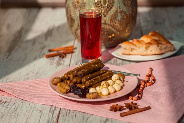 Turkish sarma on a plate with cheese, olives, pide, sorbet drink, rosary and seasonings on the table.  Photo with shallow depth of field