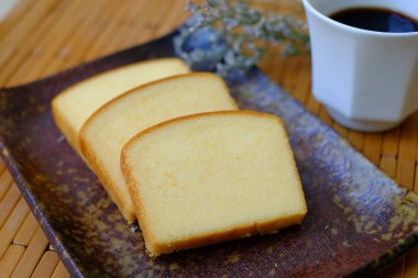 Ev yapımı düz tereyağı pasta yumuşak ve nemli. Tereyağı pasta plaka üzerinde dilim ve ahşap arka plan üzerinde siyah kahve ile hizmet