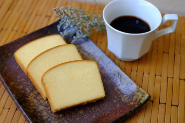 Ev yapımı düz tereyağı pasta yumuşak ve nemli. Tereyağı pasta plaka üzerinde dilim ve ahşap arka plan üzerinde siyah kahve ile hizmet