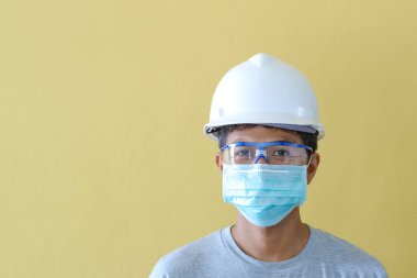 KOVID salgını karşısında güvenlik için kask ve maske takan işçiler sarı bir sahnenin önünde duruyorlar..