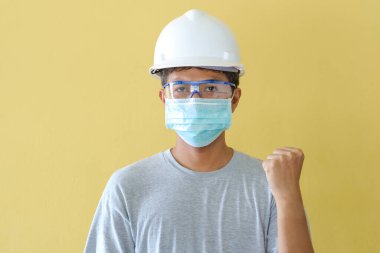 KOVID salgını karşısında güvenlik için kask ve maske takan işçiler sarı bir sahnenin önünde duruyorlar..