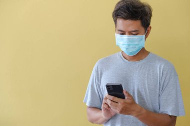 Maskeli ve cep telefonunu COVID salgını karşısında sarı bir sahnenin önünde güvenlik için kullanan adam..