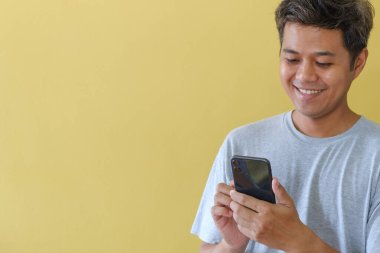 Cep telefonu kullanan ve mutlu bir şekilde gülümseyen bir adam sarı sahnenin önünde duruyor..