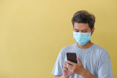 Maskeli ve cep telefonunu COVID salgını karşısında sarı bir sahnenin önünde güvenlik için kullanan adam..