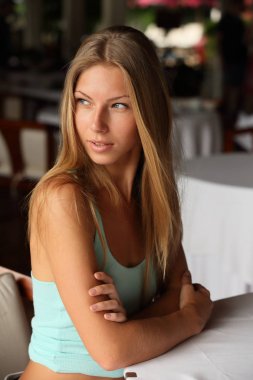 Beyaz bir masa örtüsü ile bir masada oturan güzel çıplak elleri ile çekici bir genç yetişkin sarışın kadının Portresi