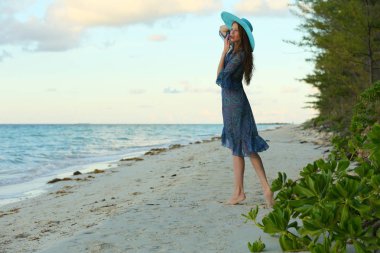 Tropik tatil gün batımında kumlu plajda poz uzun saçlı çarpıcı kızıl saçlı model