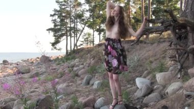 Deniz kıyısında poz veren uzun saçlı, çıplak, güzel bir kadın.