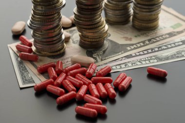 Kırmızı hapları veya kapsül dolarlarına ve koyu arka plan üzerinde paralar yığınlarının karşı. Pahalı tedavi kavramı
