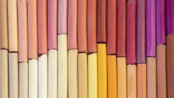 Colorful pastel crayons in warm colors in two rows as background. 16:9 format