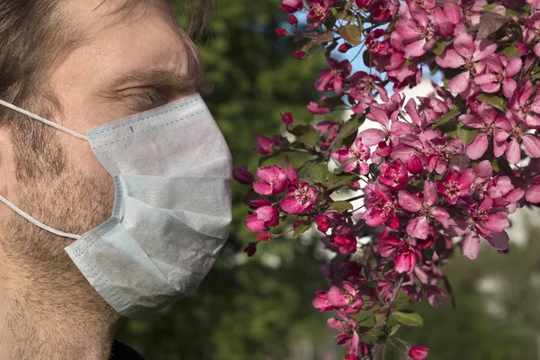 Cropped view of man with medical respirator on his face, apple-tree flowers. Lack of oxygen, weak immunity, bad ecology