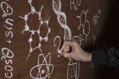 Karanlıktan bir adamın eli, formüller arasında doğaçlama bir tahtaya bir soru yazar.. 