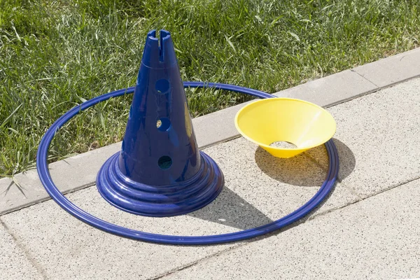 Parkta yeşil çim yakın yürüyüş yolu üzerinde mavi çember ile mavi ve sarı plastik spor koni. Oyun zamanı, spor salonu zamanı. Çocuklar için davetiye açık Oyunlar oynamak için