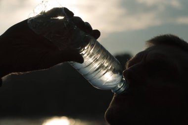 Güneşe karşı yoğun bir egzersiz den sonra bir şişeden su içen bir adamın silueti