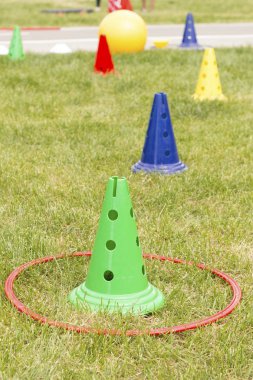 Parkta yeşil çim üzerinde kırmızı çember ile colorfull plastik spor konileri. Oynama zamanı, spor salonu zamanı. Spor koçluğu, antrenman konsepti, açık hava oyunları