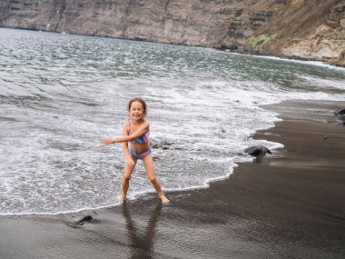 Dalgalar deniz ve kum volkanik sahilde oynarken bir plajda kız oyun. Tenerife, Kanarya Adaları