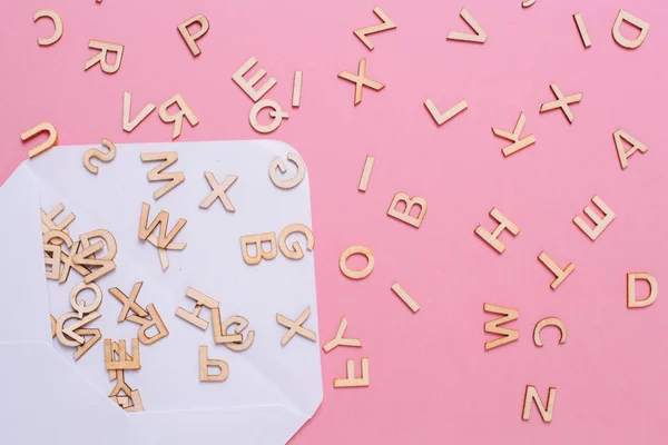 Geöffneter weißer Umschlag mit vielen Abc-Buchstaben auf rosa Hintergrund. — Stockfoto