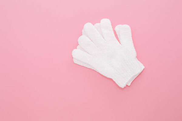 Woman exfoliating massage glove for shower on pink background.