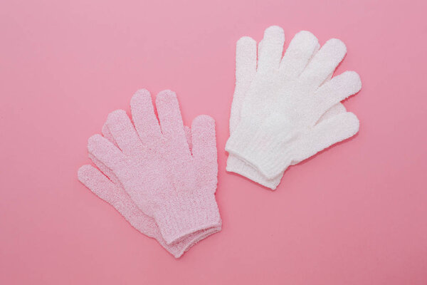 Woman exfoliating massage glove for shower on pink background.